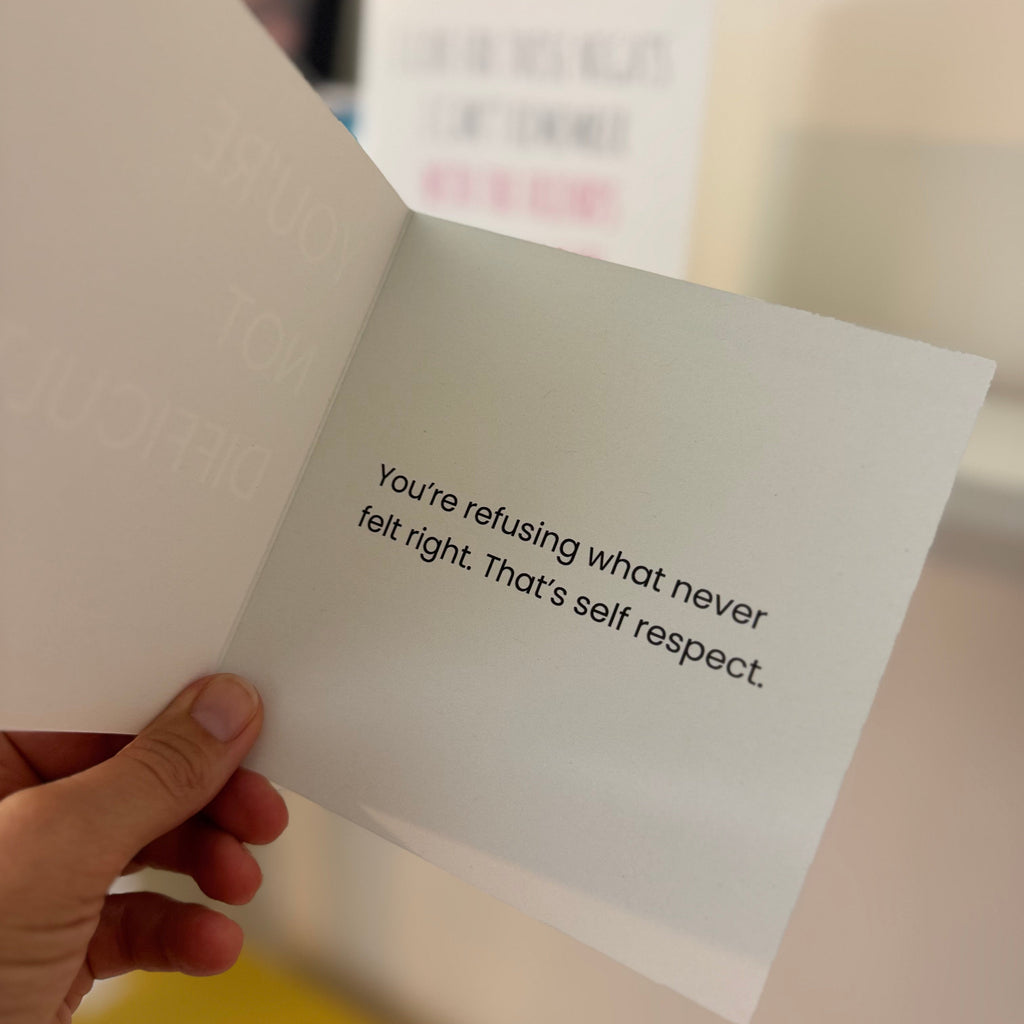 A hand holds an open white greeting card with printed black text that reads, 'You're refusing what never felt right. That's self respect.