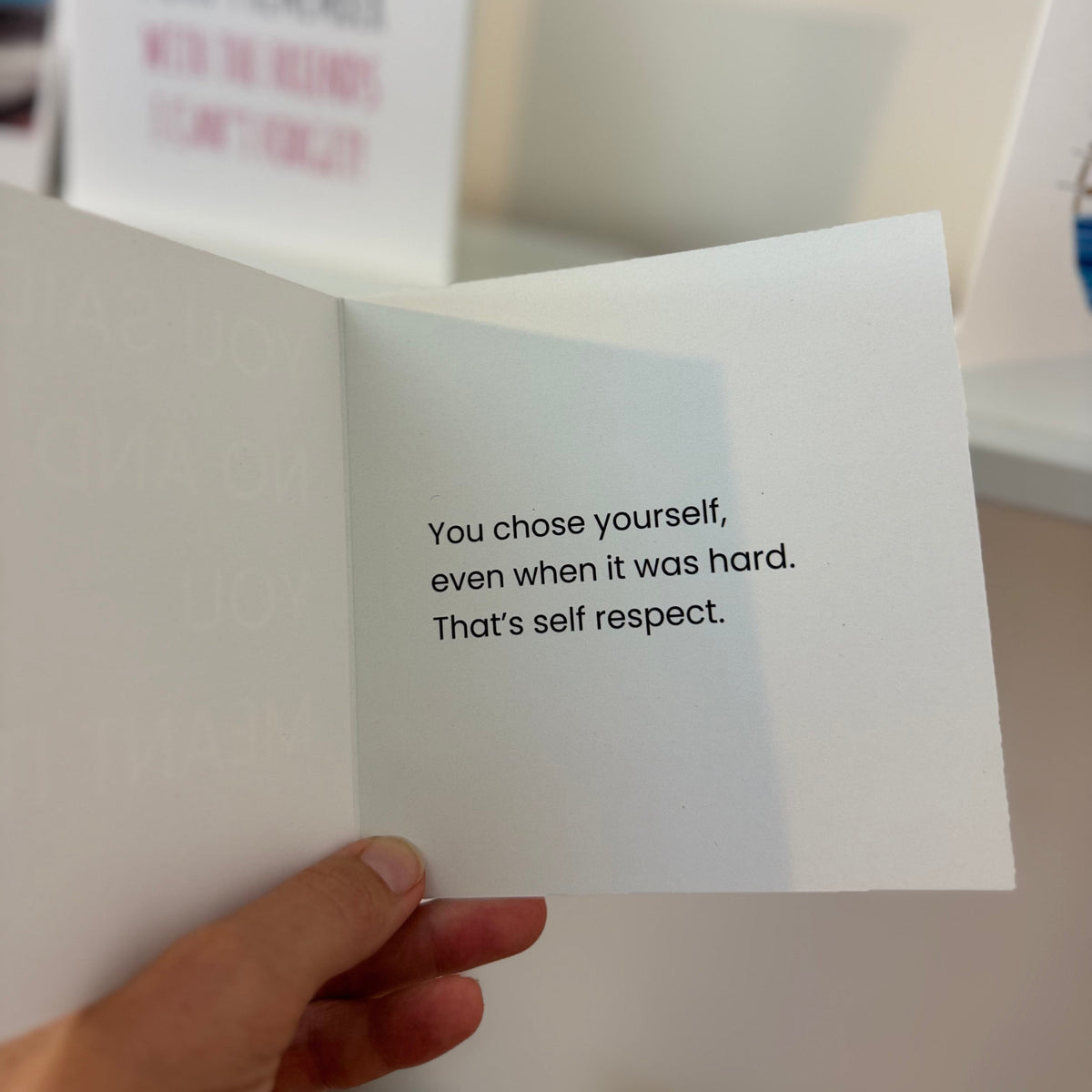 A hand holds an open white greeting card with printed black text that reads, 'You chose yourself, even when it was hard. That's self respect.