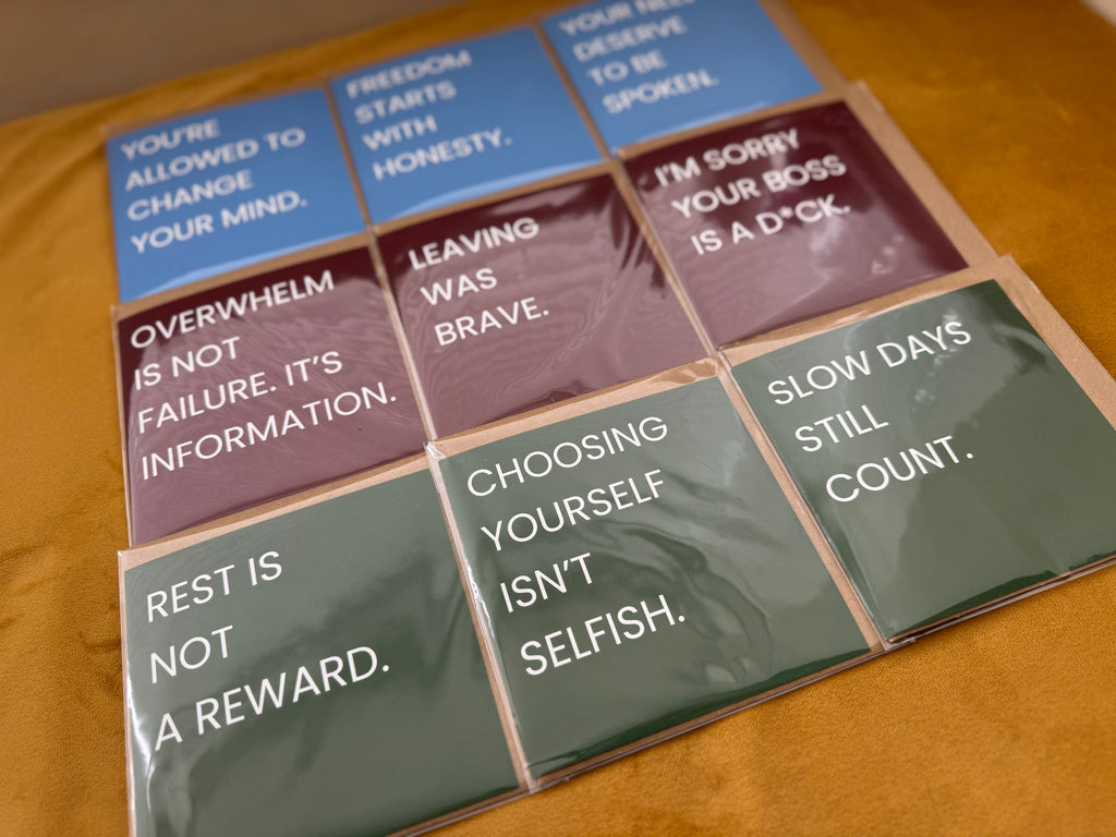 A set of quote cards arranged in a grid on a yellow surface. The cards are wrapped in clear plastic and feature different colours: blue, red, and green, with white text displaying positive affirmations.