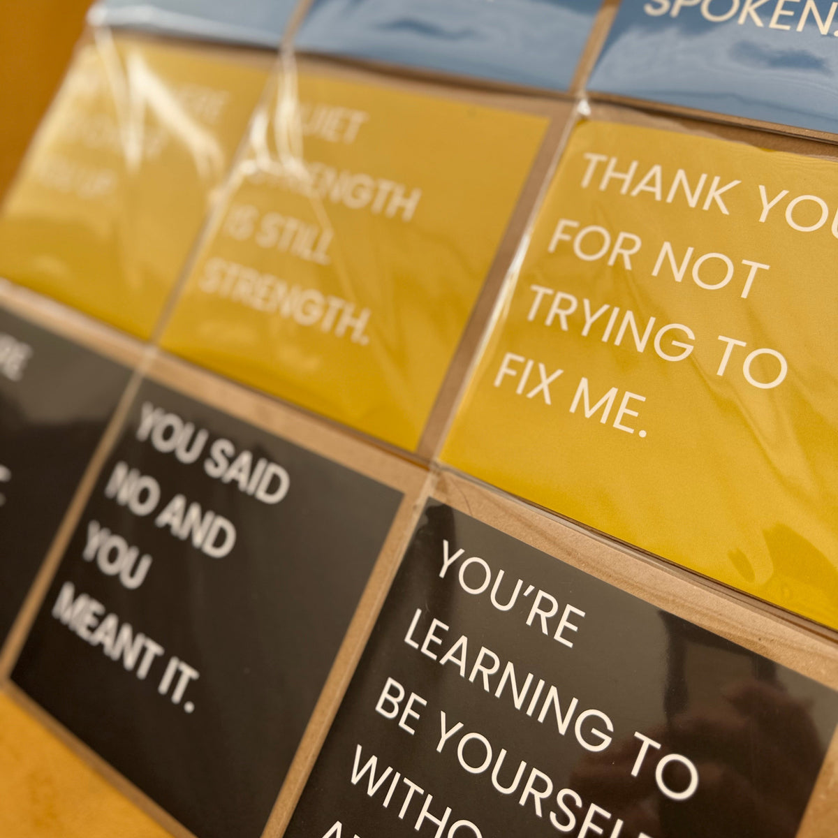 A close-up of a grid of square cards with motivational quotes in blue, yellow, and black, arranged on a wooden surface.