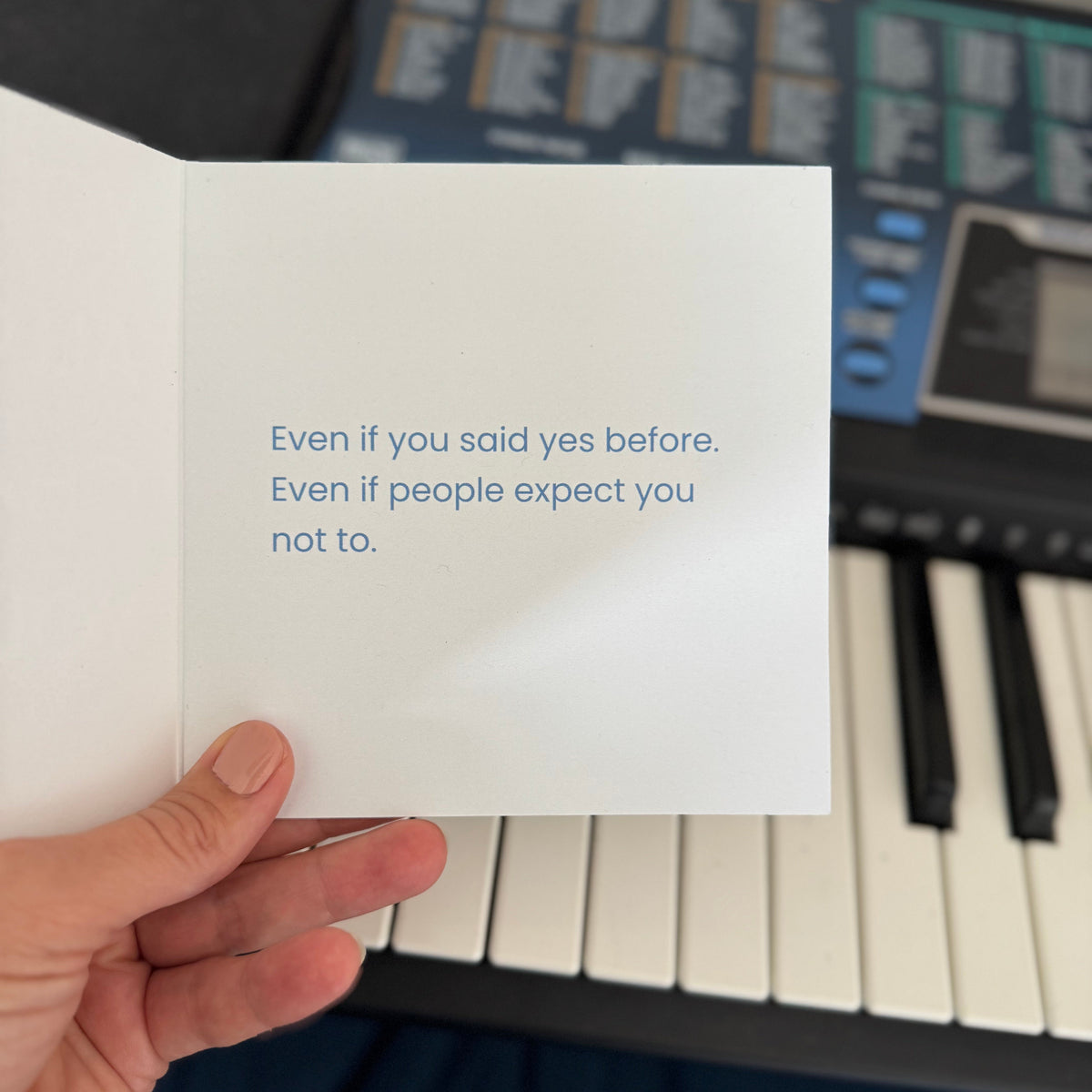 A hand holds an open white greeting card with blue text that reads, 'Even if you said yes before. Even if people expect you not to.
