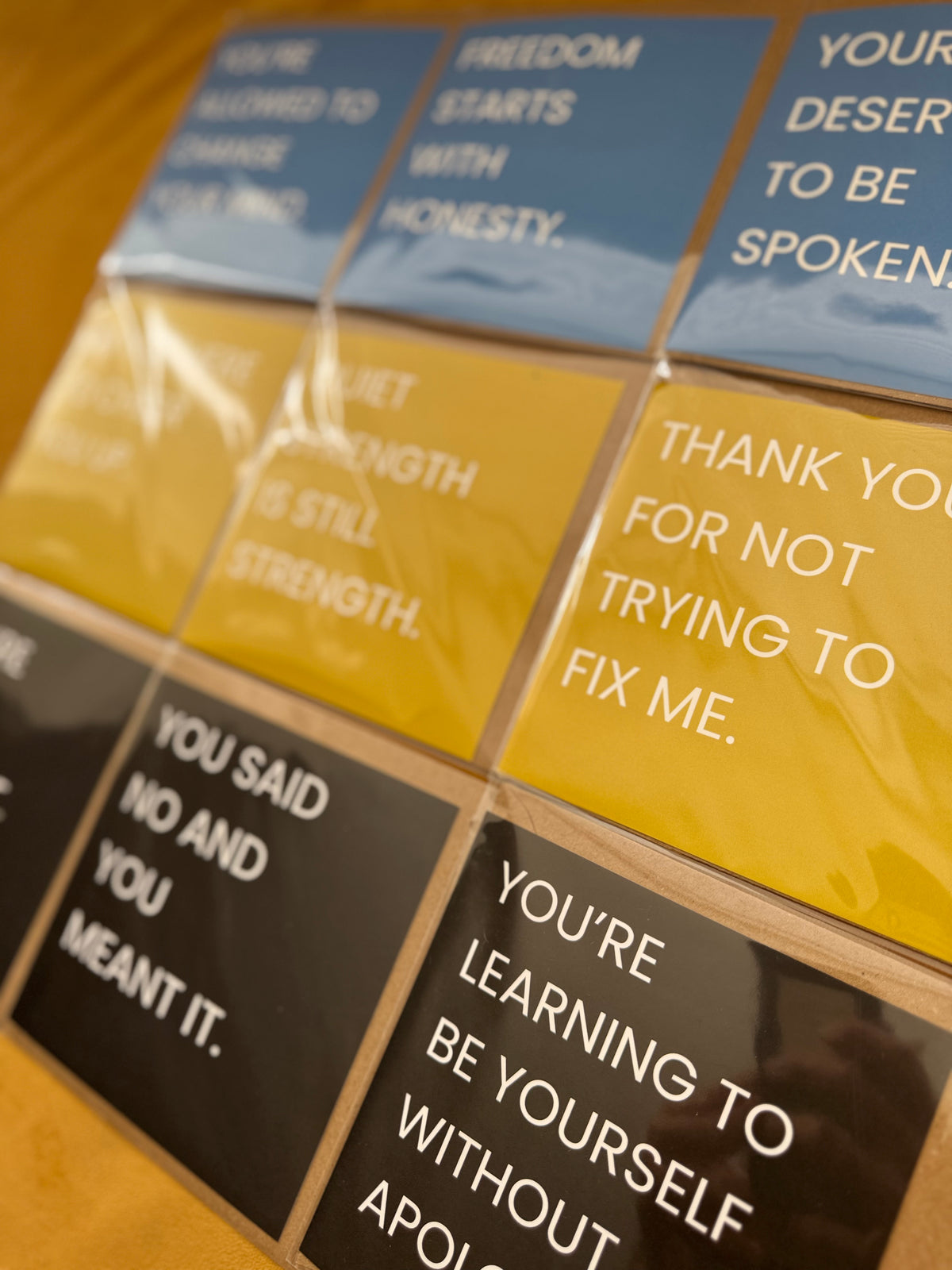 A close-up of a grid of square cards with quotes in blue, yellow, and black, arranged on a wooden surface.