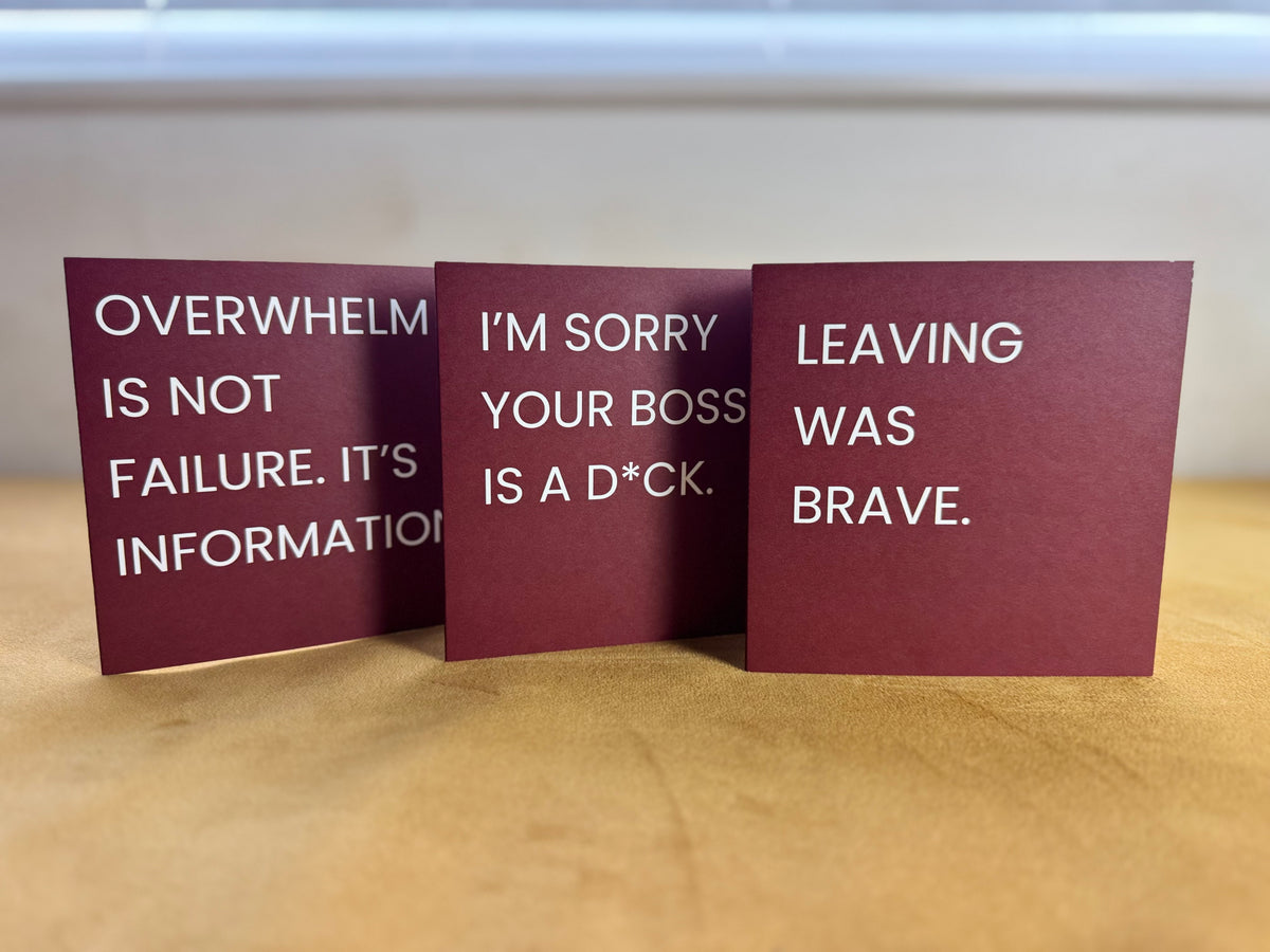 Three red greeting cards with white text displaying burnout, workplace and feelings quotes, arranged on a wooden surface.